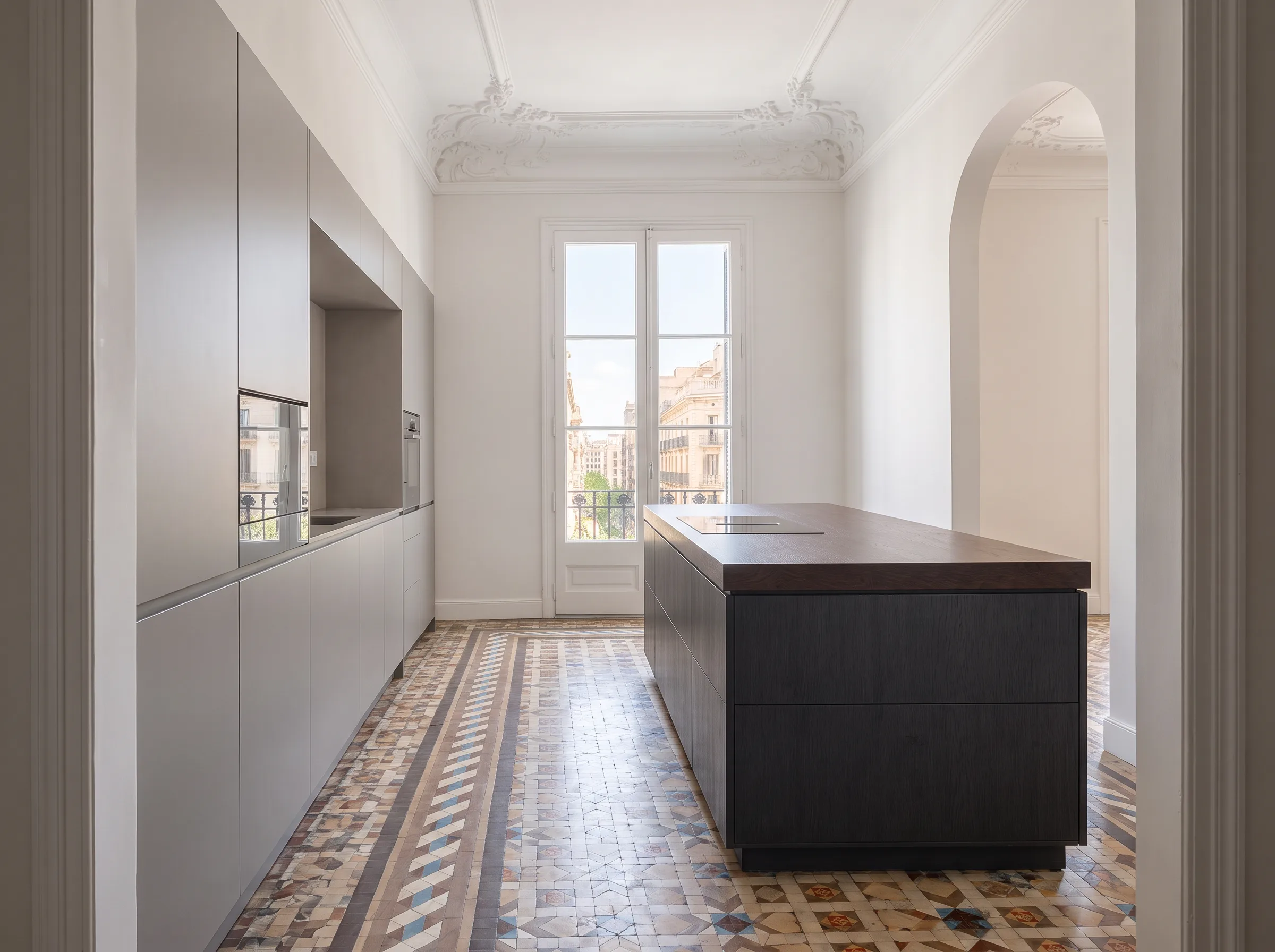 Cocina vista desde el arco: muebles grises a la izquierda, isla y balcón al fondo