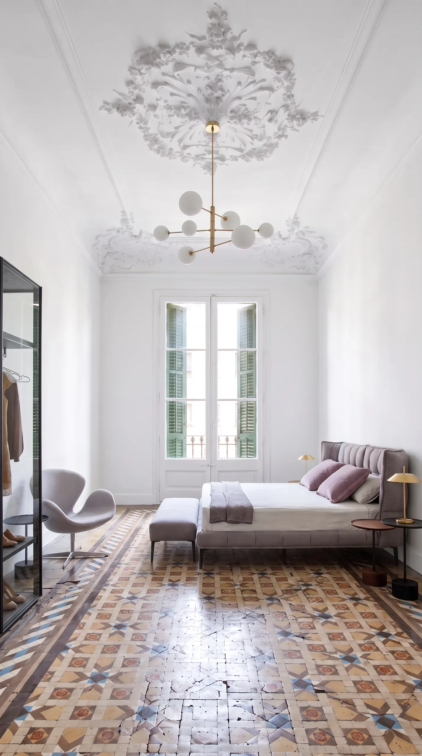 Dormitorio blanco con cama tapizada, lámpara de esferas y balcón con persianas verdes
