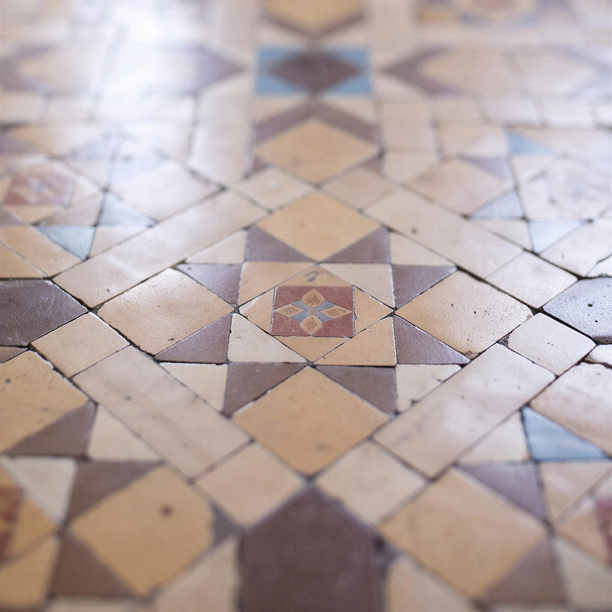 Mosaico Nolla restaurado de cerca: piezas geométricas en ocre, burdeos y azul